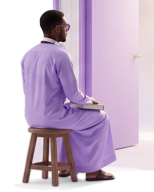 Un homme en longue tunique mauve, assis sur un petit tabouret en bois, tient un livre posé sur ses genoux près d’une porte ouverte.